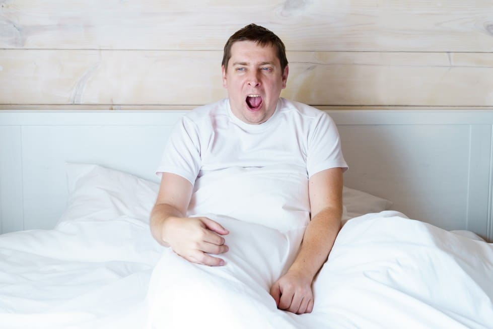 man-in-t-shirt-wakes-up-early-in-the-morning-and-yawns-in-bed-with-white-linen-in-a-wooden-bright_t20_e9Ga0o